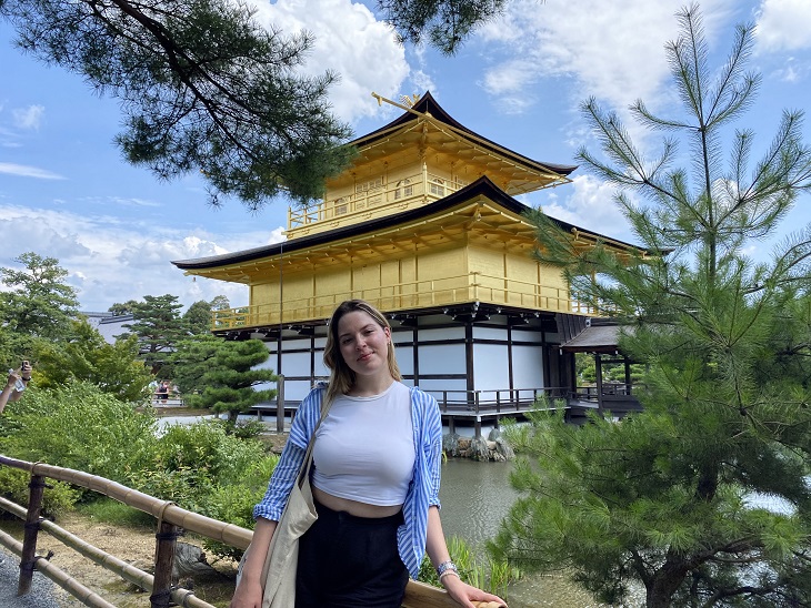Fiatal egyetemista lány kék ingben zöld növények között egy japán stílusú ház előtt