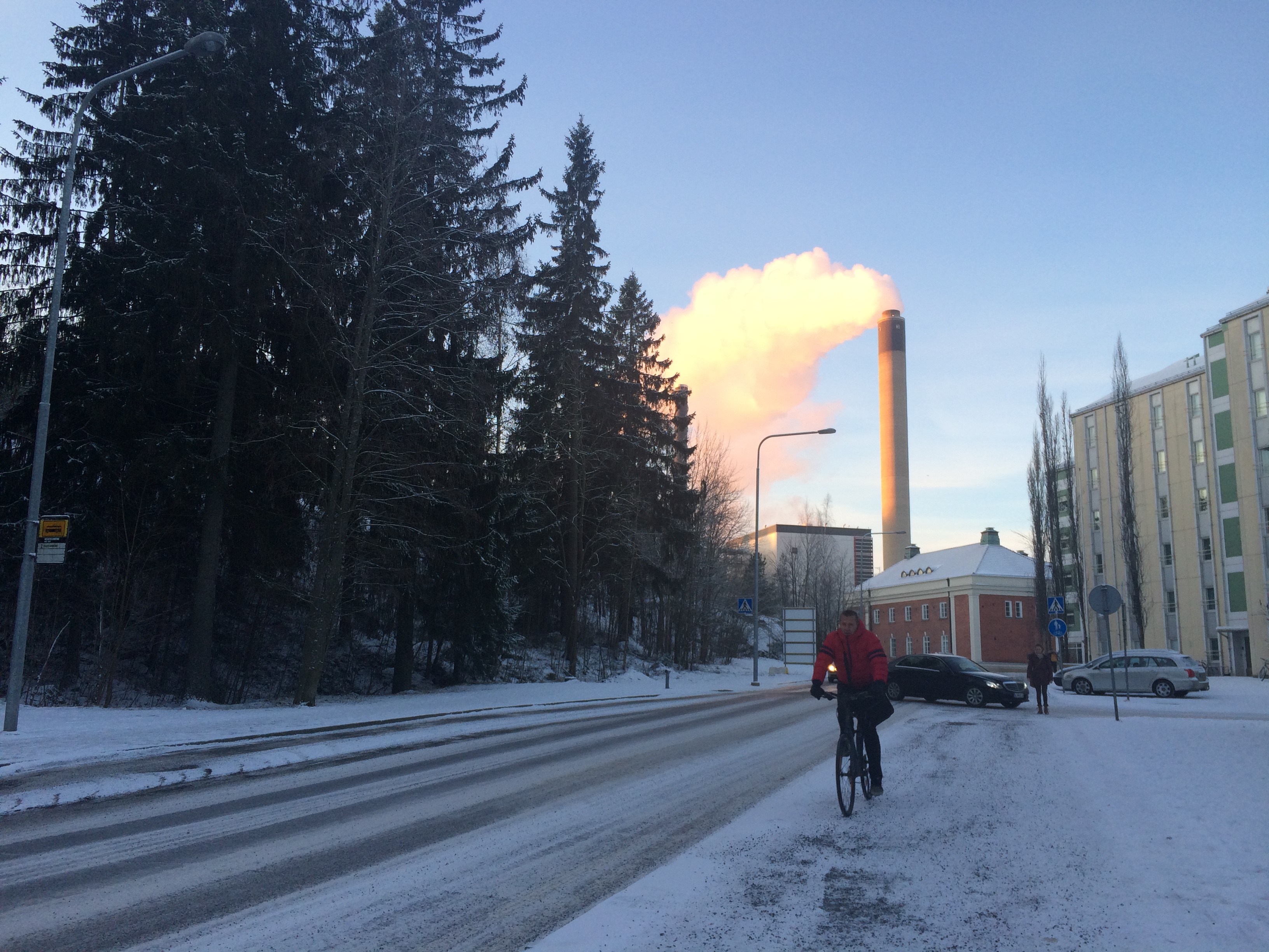 Havas utcakép ligettel házakkal gyárépülettel autókkal és egy bicikliző férfival