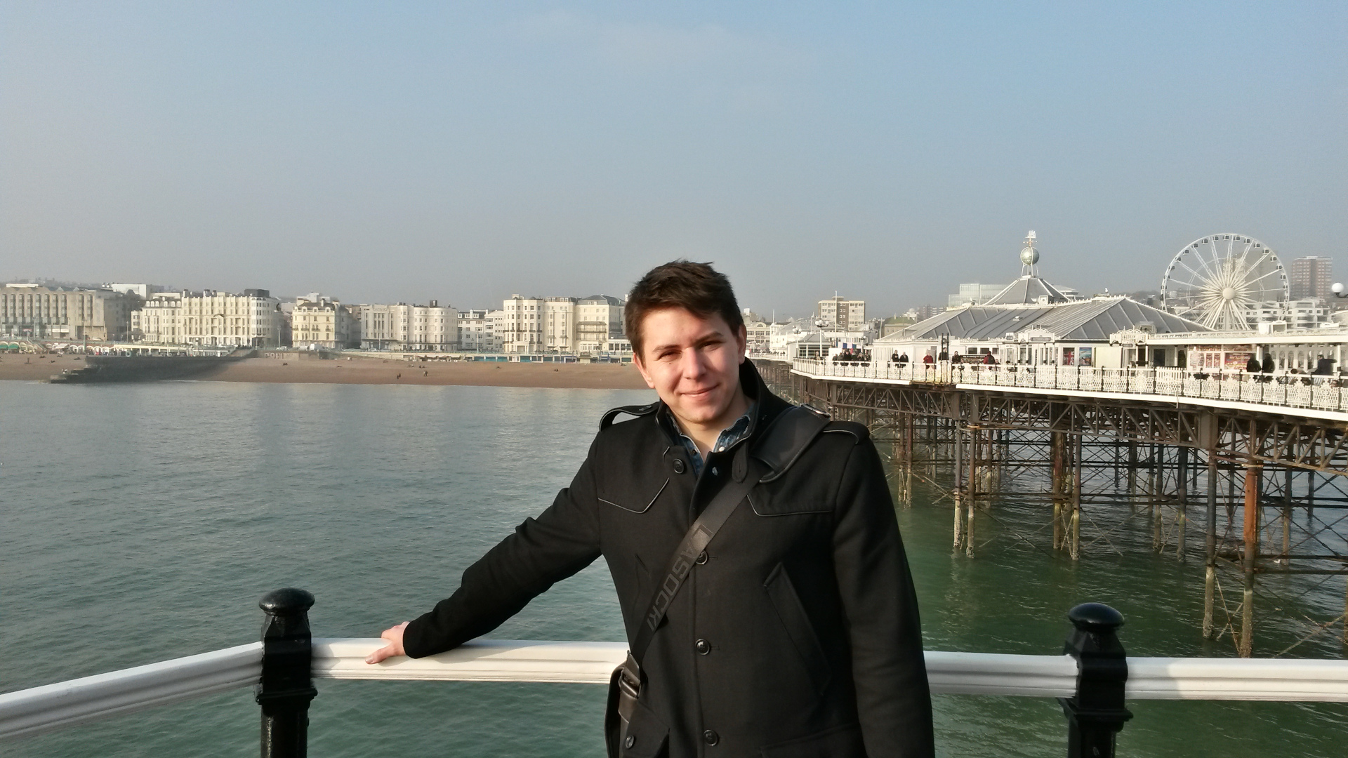 Kikötőben készült fotó ahol a móló végén áll egy fiú a háttérben látszik a cölöpökre épített móló és a környező házsorok