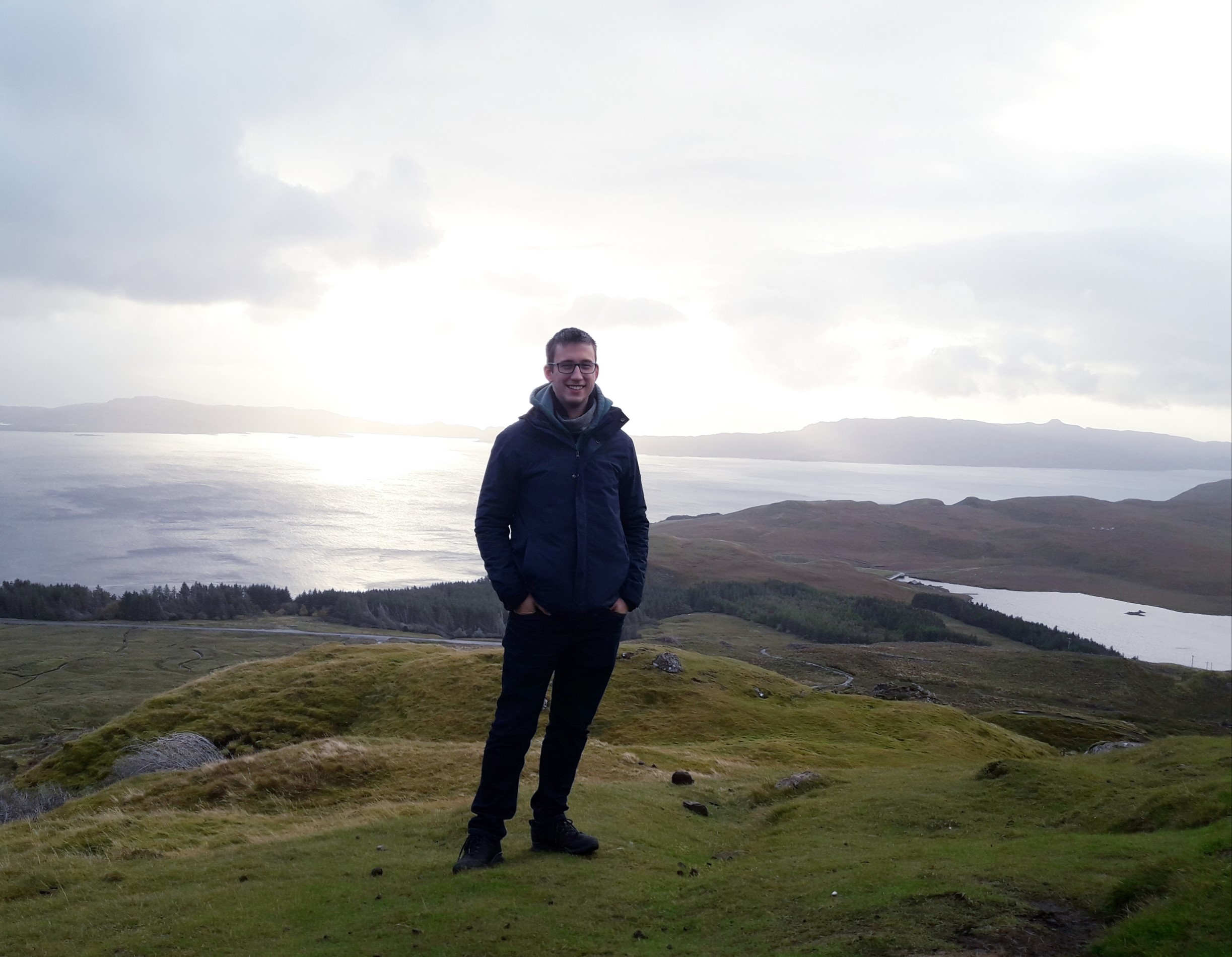 A skót felföldön húzódó Isle of Skye szigetcsoport zöldellő mezőin áll és mosolyog a kamerába egy fiatalember 